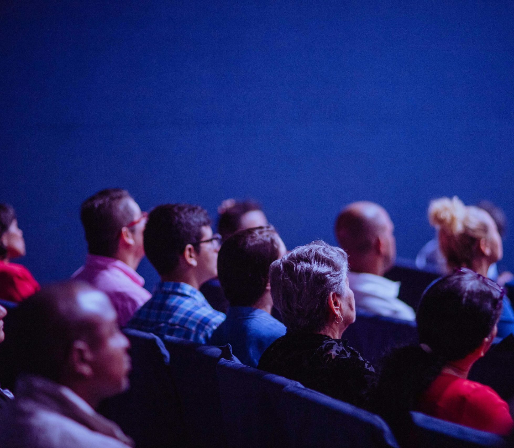 An attentive group of adults seated at an indoor conference, focusing on a presentation.